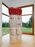 A large red and white sculpture in the corner of a gallery space with floor to ceiling windows looking out onto a field